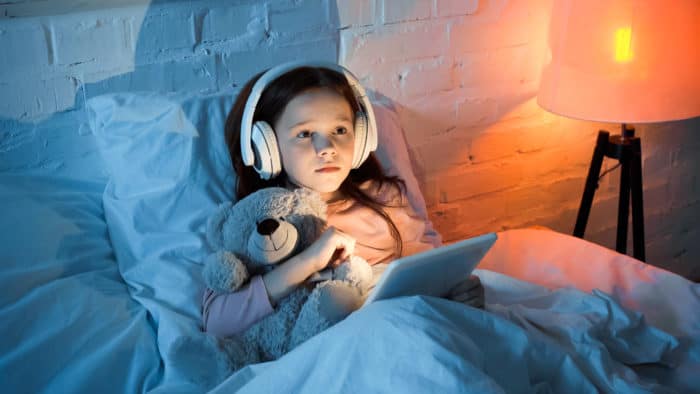 girl with teddy bear and tablet in bed